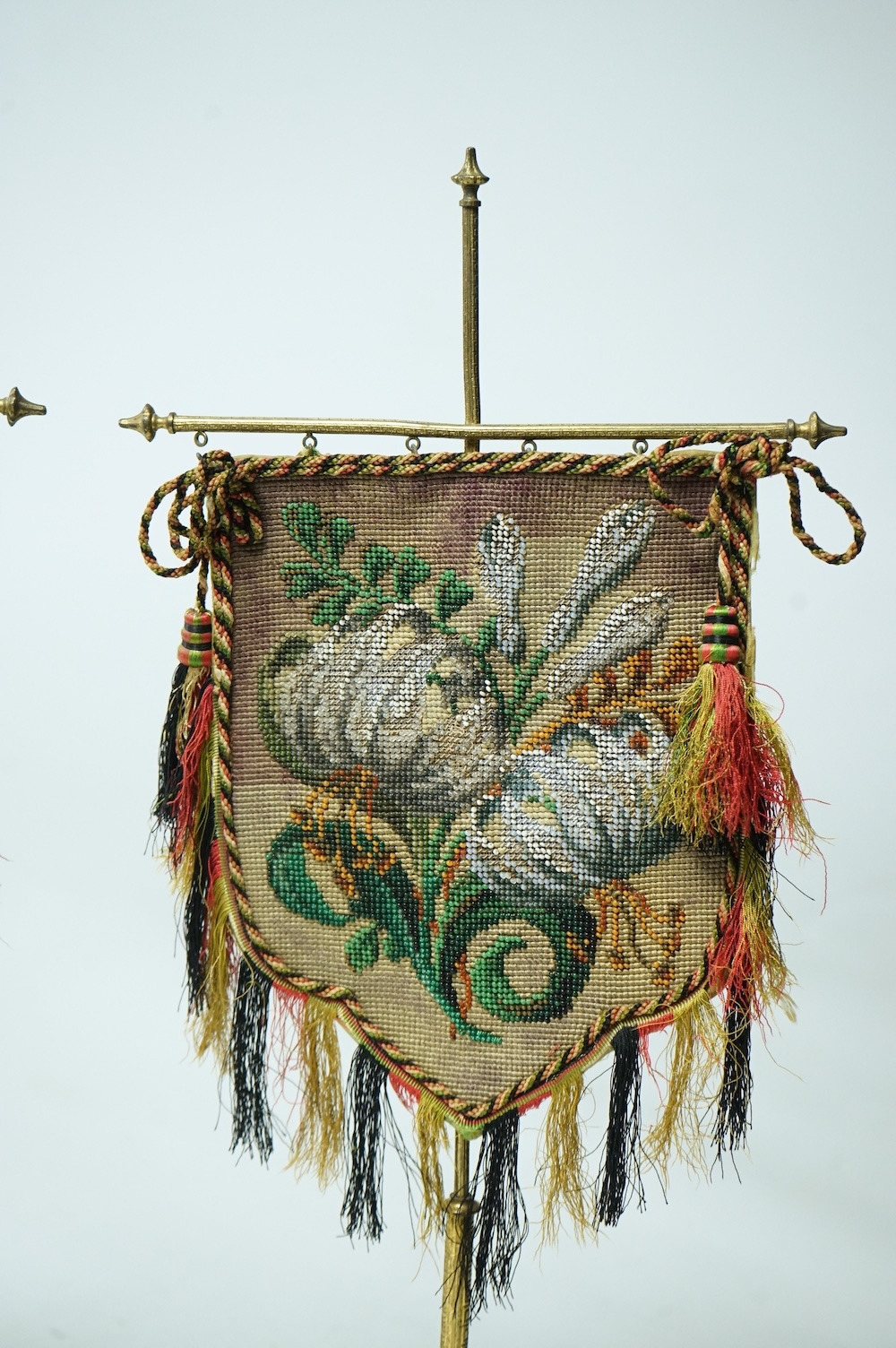 A pair of 19th century cast brass table screens, with floral Berlin Bead worked banners. 54cm high. Condition - the fringing has worn in places, silk backing has torn, both could be removed.